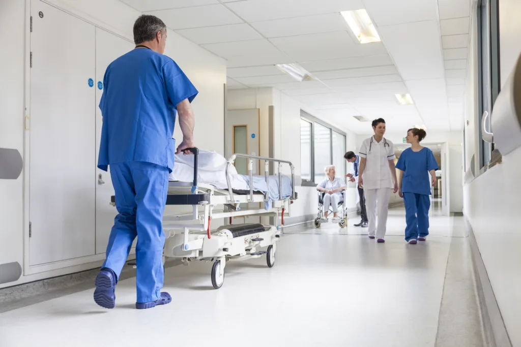 Male nurse pushing stretcher gurney bed in hospital corridor with doctors & senior female patient