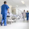 Male nurse pushing stretcher gurney bed in hospital corridor with doctors & senior female patient