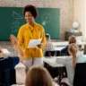 Happy African American teacher giving high-five to elementary student and congratulating him on good test results.