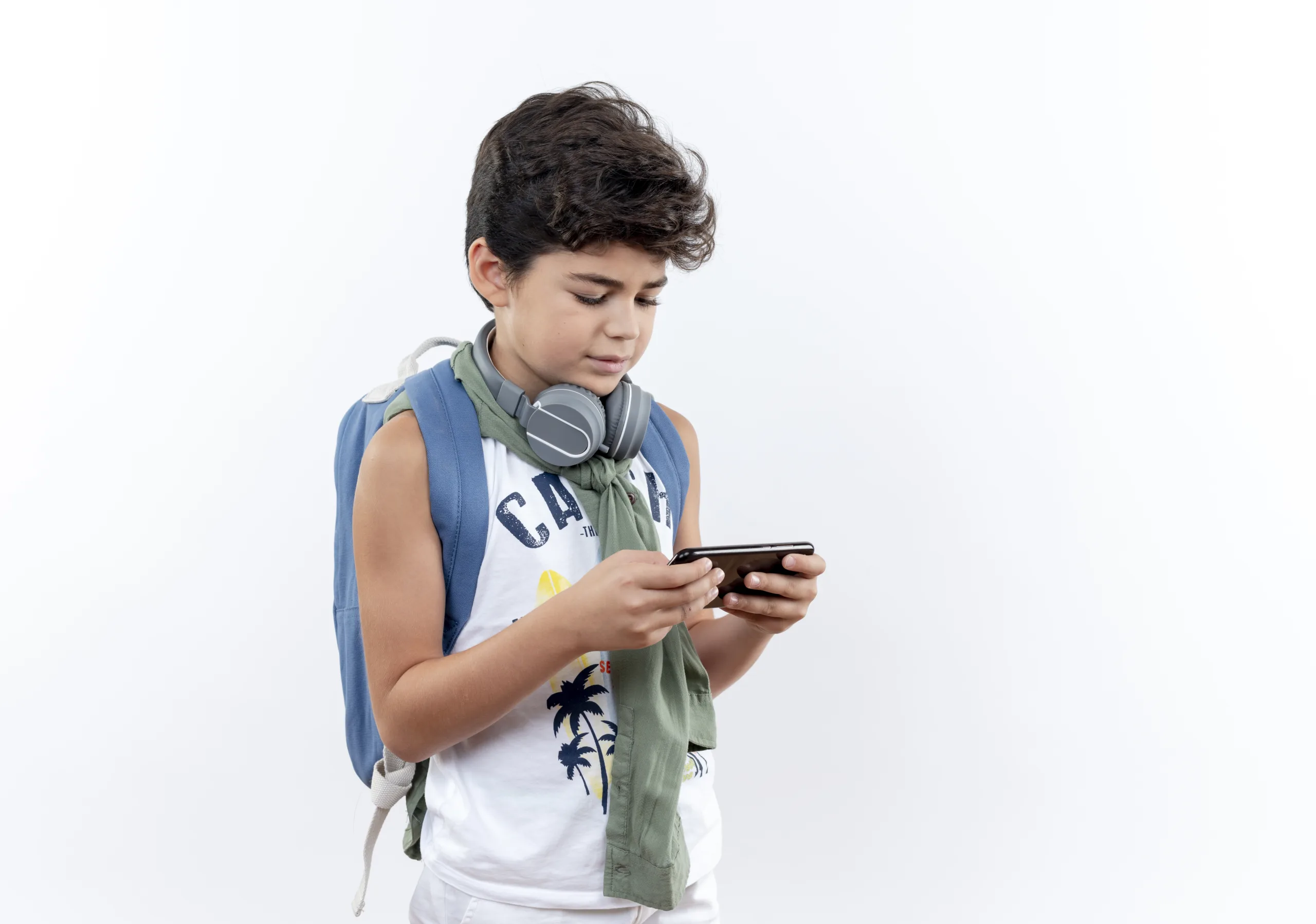 little schoolboy wearing back bag and headphones playing on phone isolated on white background with copy space