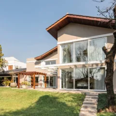 Casa moderna com fachada envidraçada, gramado e árvores. Arquitetura residencial.