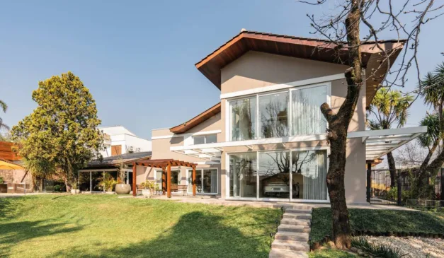 Casa moderna com fachada envidraçada, gramado e árvores. Arquitetura residencial.