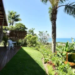 Varanda de madeira com vista para o mar e área verde exuberante.