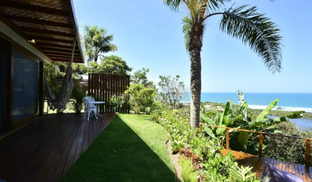 Varanda de madeira com vista para o mar e área verde exuberante.