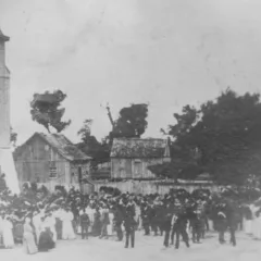 Foto antiga em preto e branco de um evento com pessoas em frente a uma igreja e edifícios.