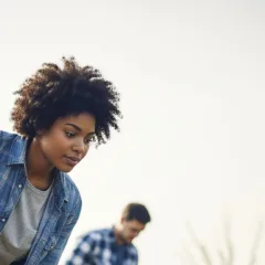 Mulher negra plantando árvore, com luva azul e camisa jeans.