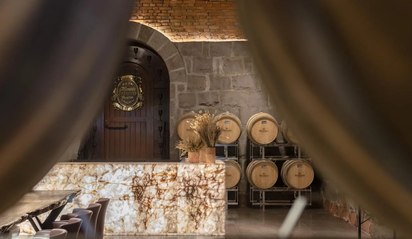 Interior de adega com barris de vinho e porta de madeira com detalhes dourados