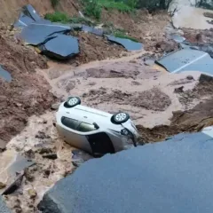 Carro capotado em deslizamento de terra após chuva forte. Estrada destruída e risco iminente.