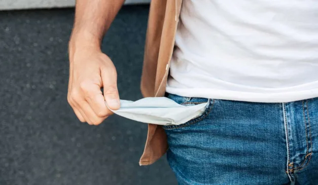Homem mostrando o bolso vazio, simbolizando falta de dinheiro ou dificuldades financeiras.