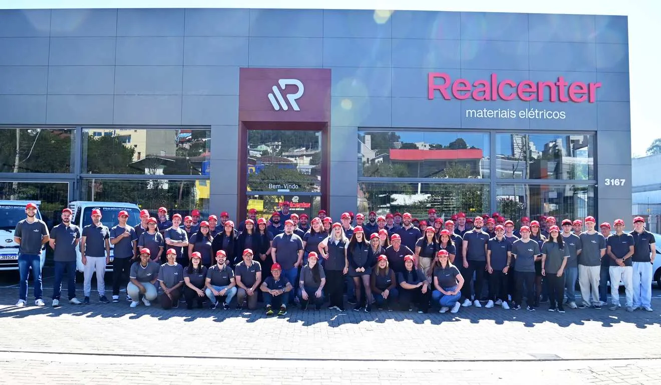 Grupo Realcenter em frente à loja, funcionários uniformizados com bonés vermelhos.