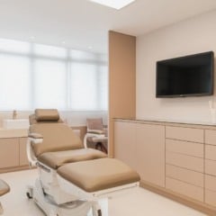Interior de consultório médico moderno e elegante, com cadeira de tratamento, TV e armários.