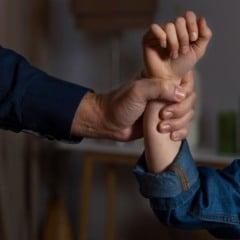 Mão de adulto segurando o braço de criança, sugerindo violência ou proteção.