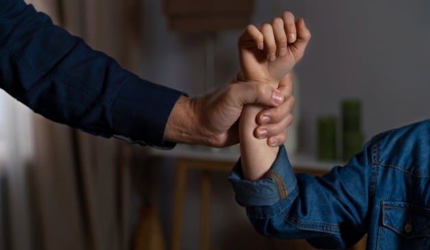 Mão de adulto segurando o braço de criança, sugerindo violência ou proteção.