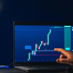 Pessoa analisa gráfico de ações em laptop, com uma lâmpada acesa