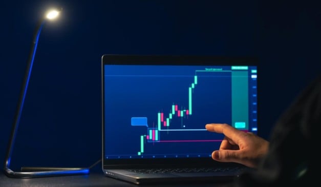Pessoa analisa gráfico de ações em laptop, com uma lâmpada acesa