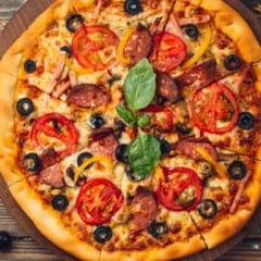 Pizza saborosa com tomate, azeitonas, salsicha e queijo em uma tábua de madeira.