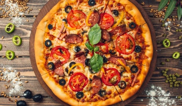 Pizza saborosa com tomate, azeitonas, salsicha e queijo em uma tábua de madeira.