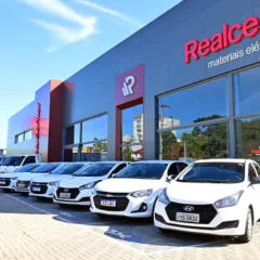 Fachada da Realcenter com carros brancos estacionados em frente, sob um céu azul.