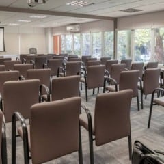 Sala de conferências com cadeiras marrons e tela de projeção.