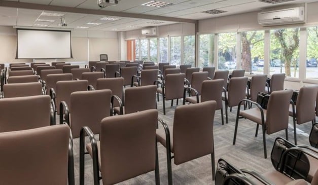 Sala de conferências com cadeiras marrons e tela de projeção.