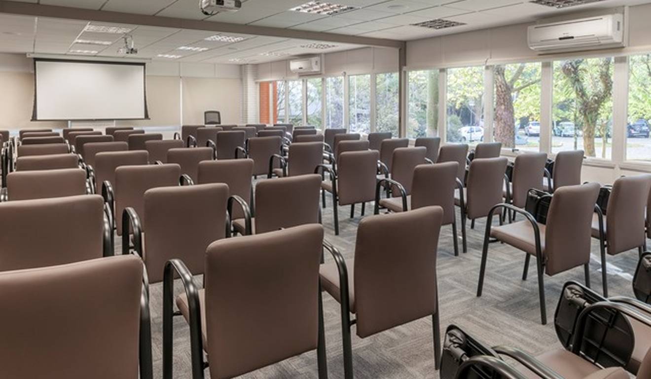Sala de conferências com cadeiras marrons e tela de projeção.