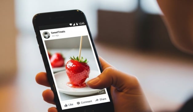 Foto de morango caramelizado em tela de celular, post de SweetTreats, mãos segurando o dispositivo