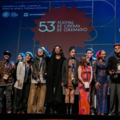 Grupo de pessoas no palco do Festival de Cinema de Gramado, incluindo premiados.
