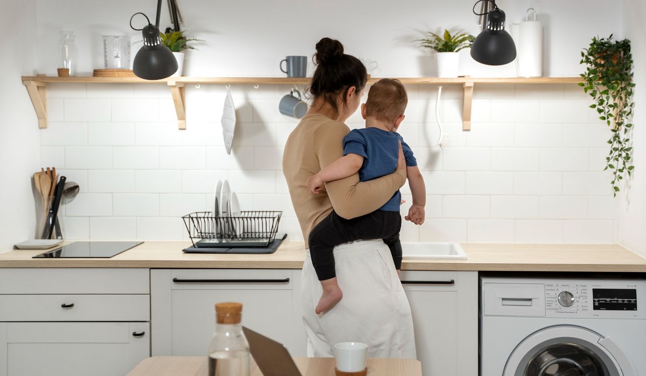 Mãe segura criança na cozinha moderna com armários brancos e eletrodomésticos.