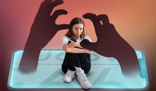 Menina sentada abraçada em um smartphone, com mãos de sombra ameaçadoras. Representação de cyberbullying.