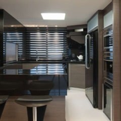 Interior de cozinha moderna com bancada preta, banquetas e eletrodomésticos.