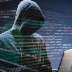 Hacker com capuz usando laptop, código em segundo plano.