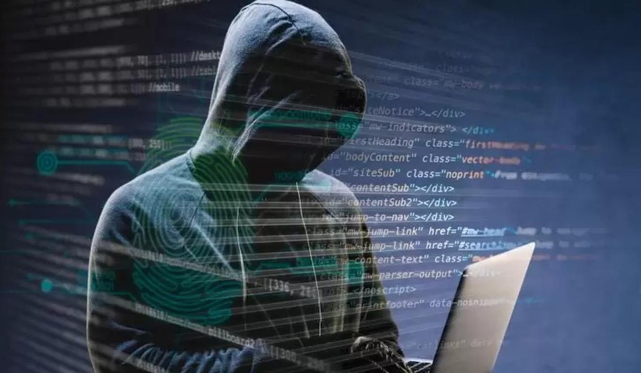 Hacker com capuz usando laptop, código em segundo plano.