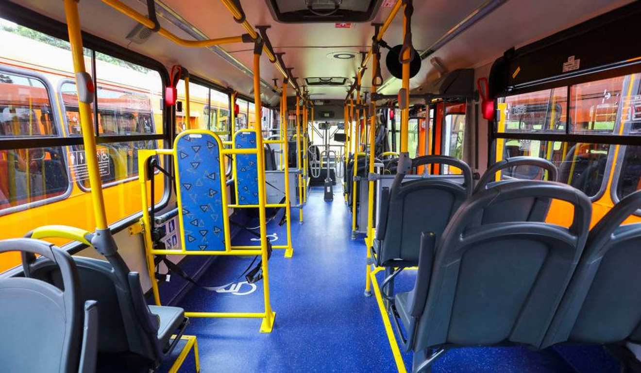 Interior de ônibus urbano, com assentos e barras amarelas, corredor azul e janelas laterais. Interior de ônibus urbano, com assentos e barras amarelas, corredor azul e janelas laterais.