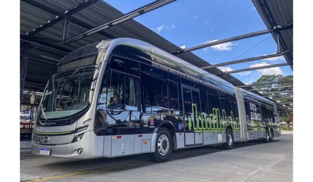 Ônibus elétrico moderno estacionado em estação, com detalhes em verde e cinza.