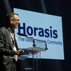 Palestrante em evento Horasis. Logotipo Horasis e slogan 'The Global Visions Community' no fundo.