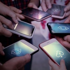 Pessoas segurando smartphones com telas mostrando ícones de nuvem e sincronização, indicando conectividade e compartilhamento de dados.
