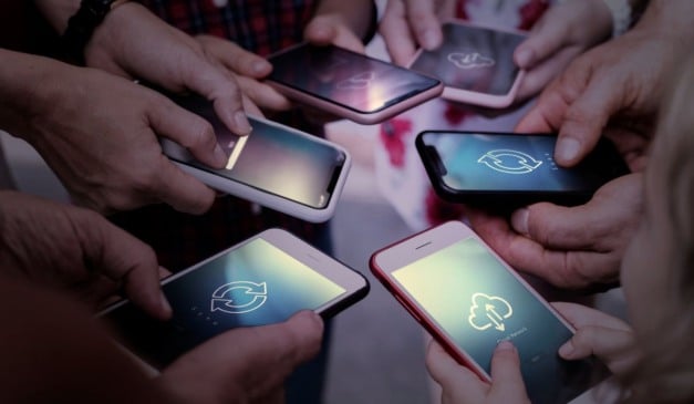 Pessoas segurando smartphones com telas mostrando ícones de nuvem e sincronização, indicando conectividade e compartilhamento de dados.