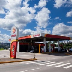 Posto de gasolina Gambino em dia ensolarado, com céu azul e nuvens brancas.