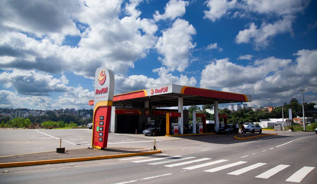 Posto de gasolina Gambino em dia ensolarado, com céu azul e nuvens brancas.