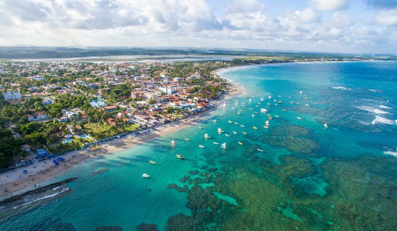 Vista aérea de uma cidade costeira com praia, mar azul e barcos à vela. Vista aérea de uma cidade costeira com praia, mar azul e barcos à vela.