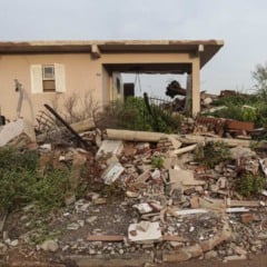 Casa destruída após desastre natural, entulho e vegetação.