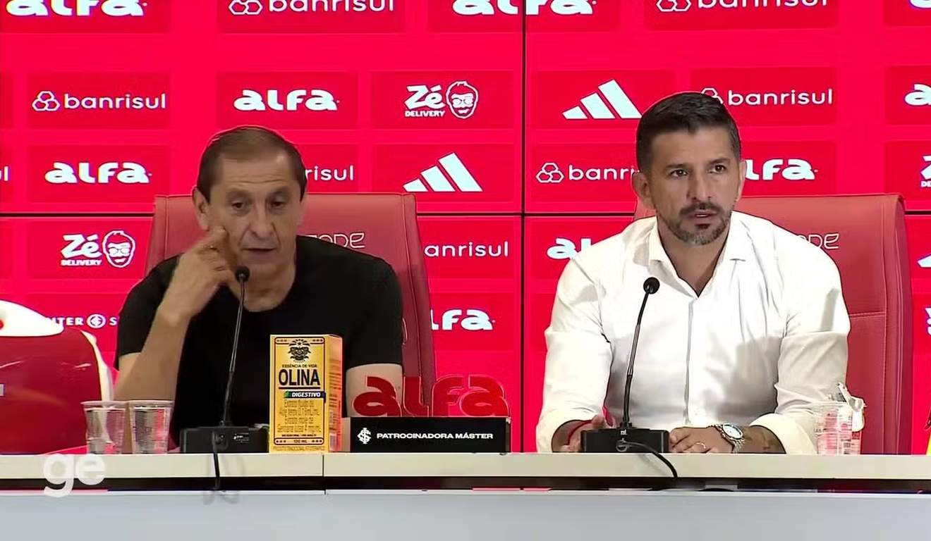 Dois homens em uma coletiva de imprensa com logotipos de patrocinadores ao fundo.