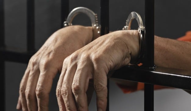 Mãos algemadas em grades de prisão.