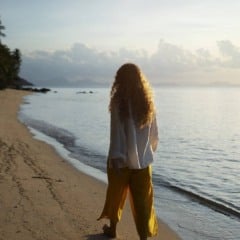 Mulher de costas na praia, contemplando o mar ao amanhecer.
