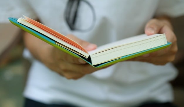 Pessoa segurando um livro aberto com bordas coloridas.