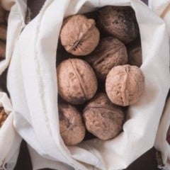 Sacos de tecido repletos de nozes, amêndoas, amendoins, avelãs e nozes descascadas, dispostos em uma superfície escura.