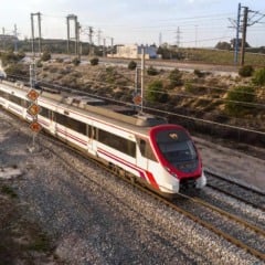 Trem de alta velocidade branco e vermelho em trilhos de trem, com sinalização de velocidade e paisagem ao fundo.