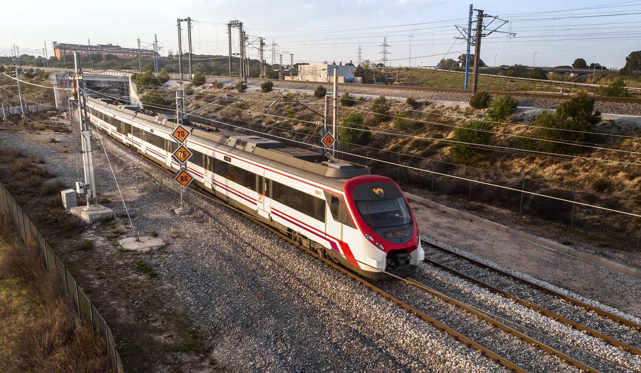 Trem de alta velocidade branco e vermelho em trilhos de trem, com sinalização de velocidade e paisagem ao fundo.