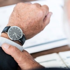 Homem de terno checando as horas em seu rel&oacute;gio de pulso.