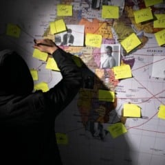 Investigador an&ocirc;nimo com mapa mundial e post-its conectados por linhas vermelhas, simulando uma investiga&ccedil;&atilde;o.